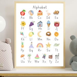 Op de afbeelding: Een rechthoekige wandposter in een lichthouten lijst met het Engelse alfabet van A tot Z. Elke letter gaat vergezeld van een kleine, kleurrijke aquarelillustratie van een object of dier, zoals een appel, een bal, een taart of een zebra.