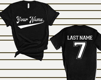 May include: Two black t-shirts with white text. The front shirt says "Your Name" in a cursive font with a white baseball-style swoosh. The back shirt says "Last Name" with the number "7" in a white block font.
