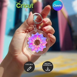 Peut inclure: Un porte-clés en acrylique transparent avec un anneau argenté. Le porte-clés présente un motif géométrique coloré avec des teintes roses, violettes et jaunes. Les logos Cricut et Canva sont visibles en arrière-plan. Le porte-clés est tenu par une personne.
