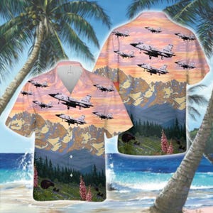 Può includere: Una camicia a maniche corte con una stampa colorata di jet da combattimento che volano sopra le montagne al tramonto. Il design include una scena di spiaggia tropicale con palme e onde oceaniche.