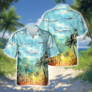 May include: A short-sleeved, button-down shirt with a tropical design. The shirt features a light blue watercolor background with white airplanes and palm trees. The design is repeated on the back of the shirt.