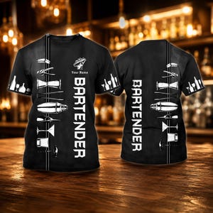 May include: A black short-sleeve t-shirt featuring a vertical white graphic of various bar tools and glassware. The text "BARTENDER" is printed vertically in white capital letters, accompanied by the text "Your Name" above the word.