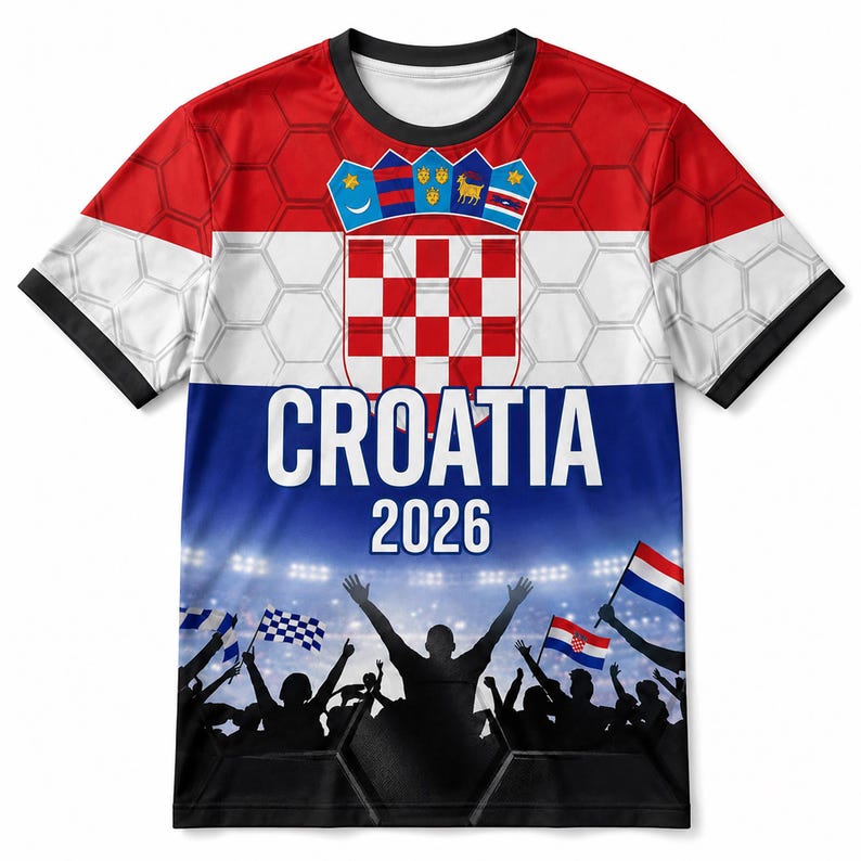 Pu&ograve; includere: Una t-shirt a maniche corte con un design rosso, bianco e blu che presenta lo stemma croato, il testo CROATIA 2026 e la grafica di una folla in festa sotto le luci dello stadio. Lo sfondo include un sottile motivo esagonale bianco.