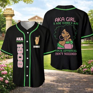 Puede incluir: Camiseta de béisbol negra con ribete verde y botones blancos. La parte delantera presenta el texto "AKA 1908" y un símbolo de mano. La parte trasera muestra un gráfico de una mujer y el texto "AKA GIRL I AM WHO I AM YOUR APPROVAL ISN'T NEEDED."