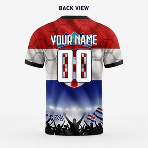 May include: A short-sleeve jersey featuring a red, white, and blue Croatian flag pattern with a honeycomb texture. The back displays the text "YOUR NAME" above the number "00" and a graphic of a cheering crowd with flags at the bottom.