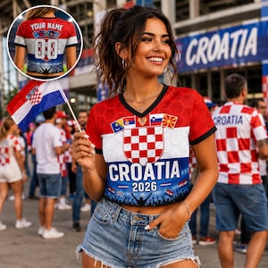 May include: A red, white, and blue V-neck crop top featuring the Croatian coat of arms, the text CROATIA 2026, and a crowd silhouette. The shirt includes a hexagonal pattern and small flags. A small circular inset shows the back with YOUR NAME and 00.