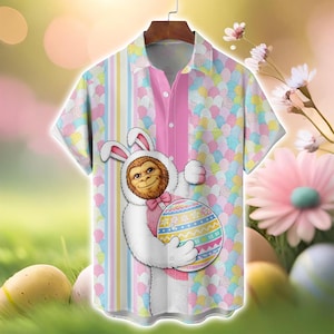 May include: Short-sleeved button-down shirt with a colorful Easter-themed design. The shirt features a cartoon Sasquatch in a bunny costume holding a decorated Easter egg. The shirt has a pink center panel and a pastel egg pattern.