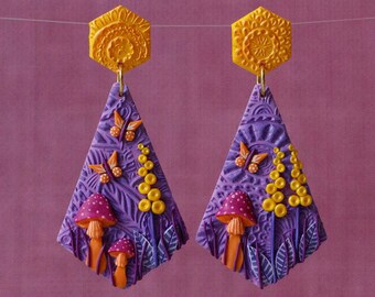 Op de afbeelding: Paarse en gele polymer clay oorbellen in de vorm van een traan met een paddenstoel-, vlinder- en bloeiende ontwerp.
