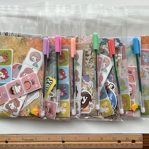 May include: A set of eight clear plastic bags containing colorful pens and stickers. The stickers feature cartoon characters and designs. The pens are rainbow colored and have a metallic finish.