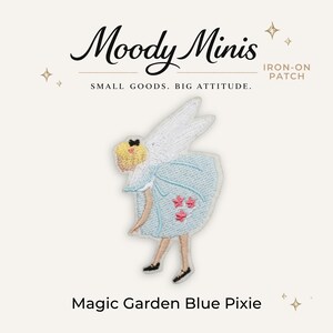 May include: An iron-on patch featuring a pixie with blonde hair, white wings, and a light blue dress adorned with three pink star-shaped flowers. The text Moody Minis, Small Goods. Big Attitude., Iron-On Patch, and Magic Garden Blue Pixie are visible.
