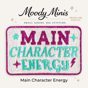 May include: A rectangular iron-on patch with a white background and a glittery magenta border. The text reads MAIN CHARACTER ENERGY in alternating glittery magenta and teal embroidered letters, accented by small teal stars and a magenta lightning bolt.