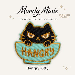 May include: An embroidered iron-on patch featuring a black cat with an angry expression inside a light blue bowl. The word HANGRY is stitched in gold thread across the bowl. The text Moody Minis, IRON-ON PATCH, SMALL GOODS. BIG ATTITUDE. and Hangry Kitty appear.