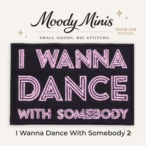 May include: A rectangular black iron-on patch featuring the embroidered light pink text I WANNA DANCE WITH SOMEBODY. The patch is displayed below the brand name Moody Minis and the text SMALL GOODS. BIG ATTITUDE. with small star icons.