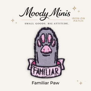 May include: An iron-on patch featuring a grey animal paw with pink pads, wrapped in a pink banner with the word FAMILIAR printed in black. Above the patch, the text reads Moody Minis, IRON-ON PATCH, and SMALL GOODS. BIG ATTITUDE. Below is Familiar Paw.