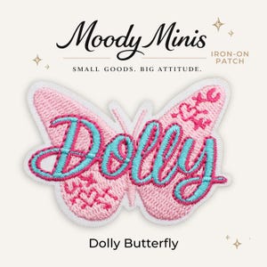 May include: An iron-on patch shaped like a butterfly with light pink embroidery. The word Dolly is stitched in bright blue cursive across the center. The wings feature small pink embroidered details including a heart and arrow motif.
