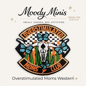 May include: An embroidered iron-on patch featuring a white cow skull centered over a black and white checkered background with green cacti and bright blue butterflies. The text reads OVERSTIMULATED MOMS CLUB in orange letters on a black border.