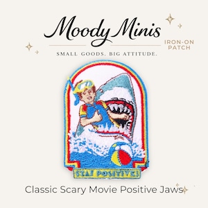 May include: An embroidered iron-on patch featuring a person wearing a snorkel and mask inside the mouth of a shark. The design includes splashing water, a colorful beach ball, and the text STAY POSITIVE in a yellow banner at the bottom.
