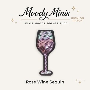 May include: An iron-on patch shaped like a wine glass, filled with iridescent pink and white sequins on a black background. The text Moody Minis, IRON-ON PATCH, SMALL GOODS. BIG ATTITUDE., and Rose Wine Sequin are printed around the patch.