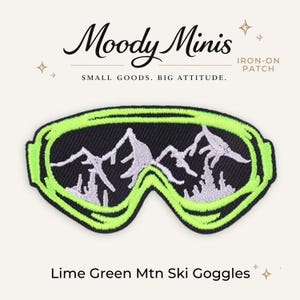 May include: An iron-on patch shaped like ski goggles with a bright lime green frame and a black lens featuring a white embroidered mountain range silhouette. The text Moody Minis, IRON-ON PATCH, SMALL GOODS. BIG ATTITUDE. and Lime Green Mtn Ski Goggles are visible.