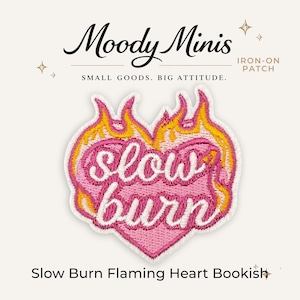 May include: An iron-on patch shaped like a heart with pink embroidery and white cursive text that reads "slow burn". The heart is surrounded by yellow and orange flames. The text "Moody Minis", "IRON-ON PATCH", "SMALL GOODS. BIG ATTITUDE.", and "Slow Burn Flaming Heart Bookish" is visible.