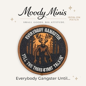 May include: A circular iron-on patch featuring a dark forest scene with a central deer-like creature. The text reads "EVERYBODY GANGSTER TILL THE TREES START TALKIN" in white lettering. The patch has a brown border and a black background.
