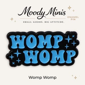 May include: An enamel pin featuring the text "WOMP WOMP" in bright blue, bubbly lettering against a black background. The design includes small four-pointed star accents. Above the pin, the text reads "Moody Minis" and "SMALL GOODS. BIG ATTITUDE."