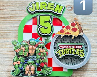 May include: A green, red, and white Teenage Mutant Ninja Turtles cake topper with four turtles, a pizza slice, and a sewer cover. The cake topper says "Jiren 5" and "Teenage Mutant Ninja Turtles Sewer".