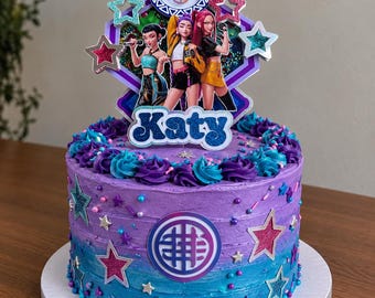 May include: A round cake with purple and blue ombre frosting, decorated with colorful sprinkles and star cutouts. A large topper features three female characters, a circular logo, and the name Katy in blue glittery script lettering.