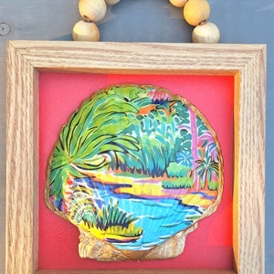 May include: A framed seashell with a painted tropical scene inside. The shell is gold and the scene is colorful with green palm trees, blue water, and a sandy beach.
