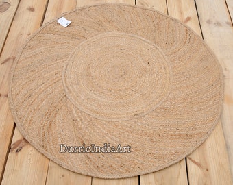 May include: A round, natural fiber rug with a woven design. The rug is made of jute and has a natural beige color. The rug is approximately 3 feet in diameter. The text "DurrieIndiaArt" is printed on the rug.