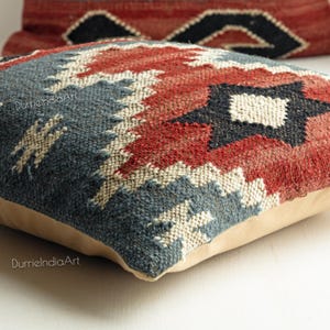 May include: A blue, red, and white patterned throw pillow with a beige backing. The pillow is made of woven fabric and has a geometric design.