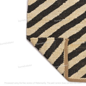 May include: Close-up of a black and natural jute rug with diagonal stripes. The rug has a natural jute border.