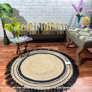 May include: A round jute rug with black stripes and black fringe. The rug is on a wooden floor with a bench and a stool in the background.