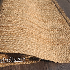 Pode incluir: Um tapete de fibra natural feito de juta, um material sustent&aacute;vel e dur&aacute;vel. O tapete tem uma textura tecida e uma cor bege natural. O tapete est&aacute; enrolado e a borda &eacute; vis&iacute;vel. O texto "DurrieIndiaArt" &eacute; vis&iacute;vel no tapete.