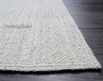 May include: A white woven jute rug with a braided edge. The rug is made of natural fibers and has a textured surface.