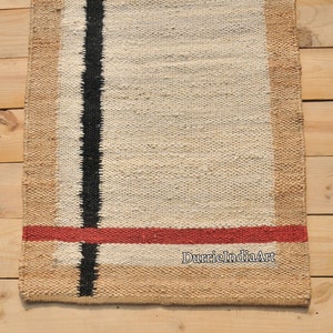 May include: A white and beige handwoven rug with black and red stripes. The rug has a natural jute border. The text "DurrieIndiaArt" is visible in the bottom right corner.