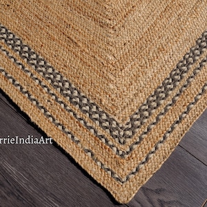May include: A natural fiber rug with a woven design. The rug has a brown and beige color with a black border. The border has a braided design.