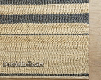 May include: A natural fiber rug with a striped pattern in beige and dark gray. The rug is woven with a textured surface and has a simple, modern design. The text "DurrieIndiaArt" is visible in the lower left corner of the rug.