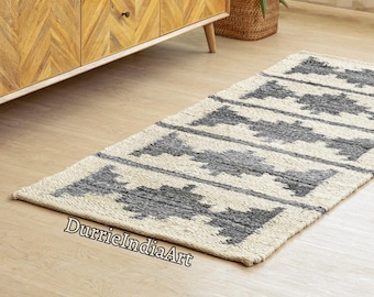 May include: A rectangular woven runner rug featuring a natural cream-colored base with repeating dark gray geometric diamond patterns arranged in horizontal rows. The rug has a textured, fibrous appearance and is positioned on a light wood floor.