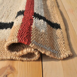 May include: A close-up of a woven jute rug with black, white, and red stripes. The rug is folded over, showing the texture of the jute fibers. The text "DurrieIndiaArt" is visible on the rug.