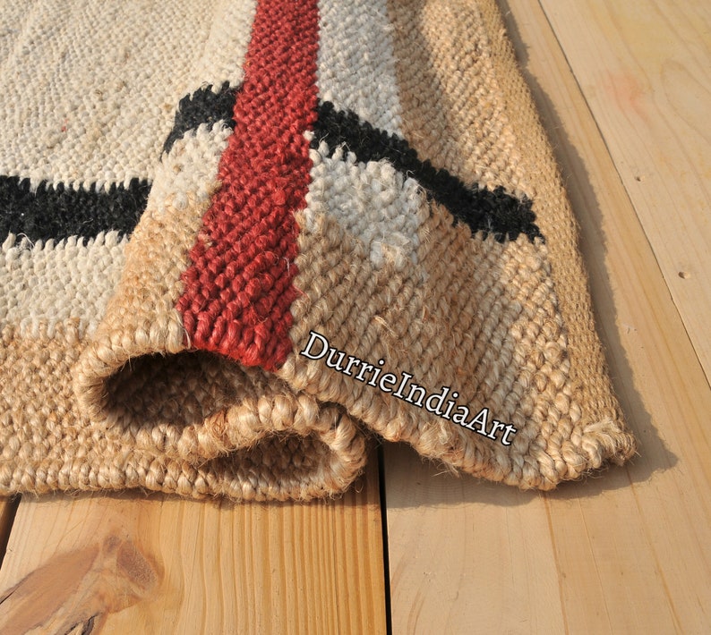 May include: A close-up of a woven jute rug with black, white, and red stripes. The rug is folded over, showing the texture of the jute fibers. The text "DurrieIndiaArt" is visible on the rug.
