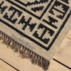 Puede incluir: Alfombra geom&eacute;trica en blanco y negro con flecos. La alfombra est&aacute; hecha de fibras naturales y tiene un aspecto r&uacute;stico.