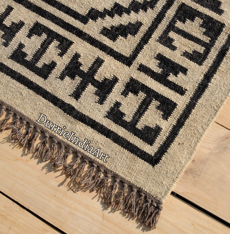 Puede incluir: Alfombra geom&eacute;trica en blanco y negro con flecos. La alfombra est&aacute; hecha de fibras naturales y tiene un aspecto r&uacute;stico.