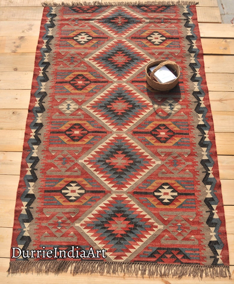 May include: A red, blue, and beige patterned rug with a geometric design. The rug has fringe on the edges and is made of wool.