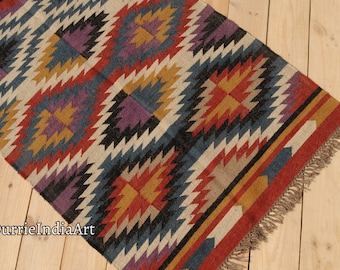 May include: A colorful geometric patterned rug with a fringe border. The rug features shades of red, orange, yellow, blue, purple, and black.