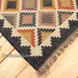May include: A black and white geometric patterned rug with a fringe border. The rug has a cream background with black, brown, orange, and yellow geometric shapes.