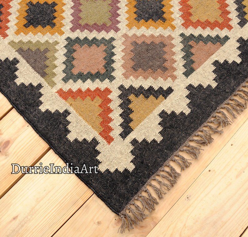 May include: A black and white geometric patterned rug with a fringe border. The rug has a cream background with black, brown, orange, and yellow geometric shapes.