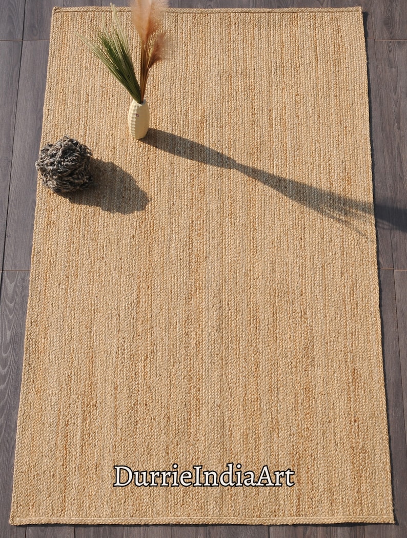 Pode incluir: Um tapete de fibra natural feito de juta, um material sustent&aacute;vel e dur&aacute;vel. O tapete tem uma cor castanho claro e uma textura tecida. O tapete &eacute; perfeito para adicionar um toque de beleza natural a qualquer divis&atilde;o.