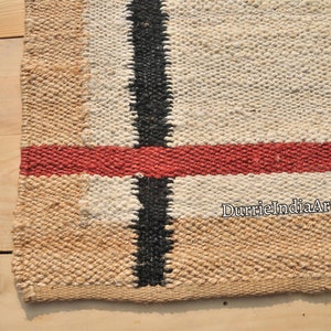 May include: A close-up of a woven rug with a black, red, and white striped pattern. The rug is made of natural fibers and has a rustic look. The text "DurrieIndiaArt" is visible in the lower right corner.