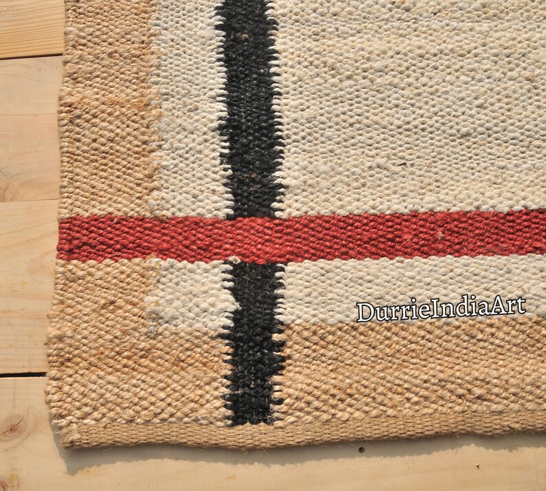 May include: A close-up of a woven rug with a black, red, and white striped pattern. The rug is made of natural fibers and has a rustic look. The text "DurrieIndiaArt" is visible in the lower right corner.